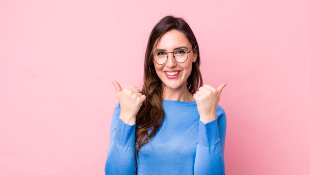 Sonriendo alegremente y luciendo feliz sintiéndose despreocupado y positivo con ambos pulgares hacia arriba