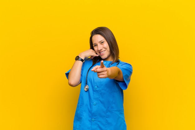 Sonriendo alegremente y señalando mientras haces una llamada, luego haces un gesto, hablando por teléfono aislado contra la pared amarilla