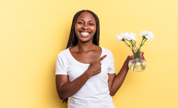 Sonriendo alegremente, sintiéndose feliz y apuntando hacia un lado y hacia arriba, mostrando el objeto en el espacio de la copia. concepto de flores decorativas