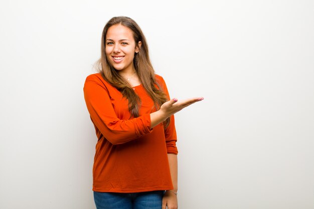 sonriendo alegremente, sintiéndose feliz y mostrando un concepto en el espacio de la copia con la palma de la mano