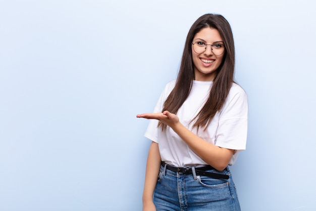 sonriendo alegremente, sintiéndose feliz y mostrando un concepto en el espacio de la copia con la palma de la mano