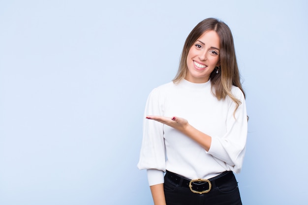 sonriendo alegremente, sintiéndose feliz y mostrando un concepto en el espacio de la copia con la palma de la mano