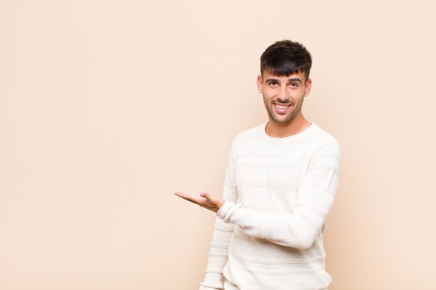 sonriendo alegremente, sintiéndose feliz y mostrando un concepto en el espacio de la copia con la palma de la mano