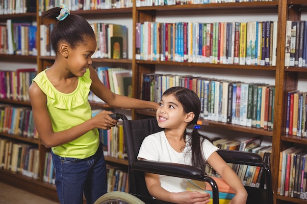 Sonriendo alumno en silla de ruedas con libros en la biblioteca