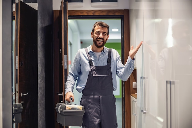 Foto sonriendo amable reparador entrando en la casa, sosteniendo una caja con herramientas y está listo para arreglar cosas en la casa.