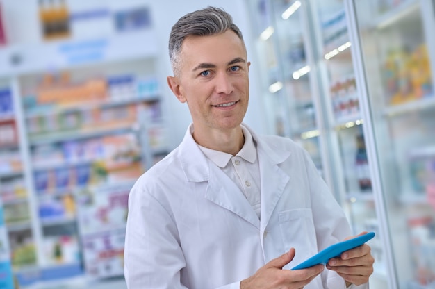 Sonriendo en bata médica con tableta en farmacia