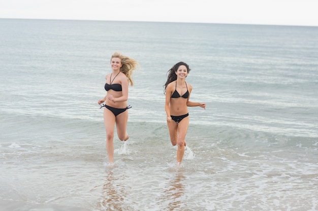 Sonriendo bikini mujeres corriendo en el agua en la playa