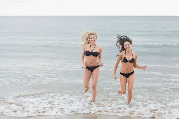 Sonriendo bikini mujeres corriendo en el agua en la playa