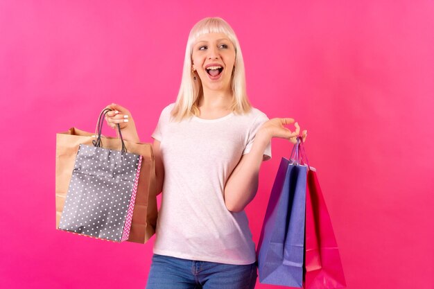 Foto sonriendo con bolsas de compras a la venta chica rubia caucásica en estudio sobre fondo rosa