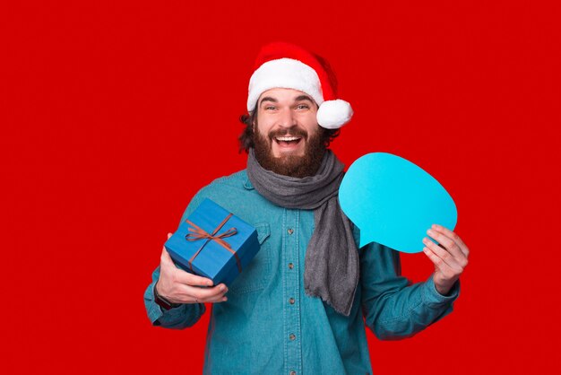 Sonriendo a la cámara, el hombre sostiene una caja de regalo y un bocadillo azul.