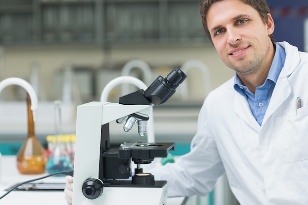 Sonriendo científico investigador con microscopio en laboratorio