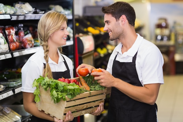 Sonriendo colegas sosteniendo una caja con verduras frescas