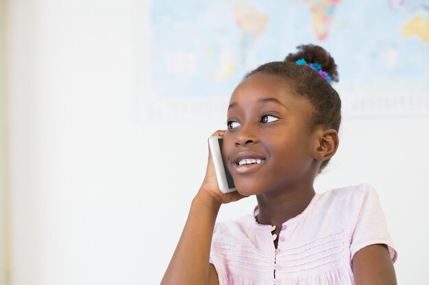 Sonriendo colegiala hablando por teléfono móvil en el aula