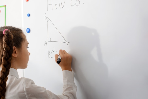 Sonriendo colegiala haciendo tarea de geometría matemática en marcador blanco