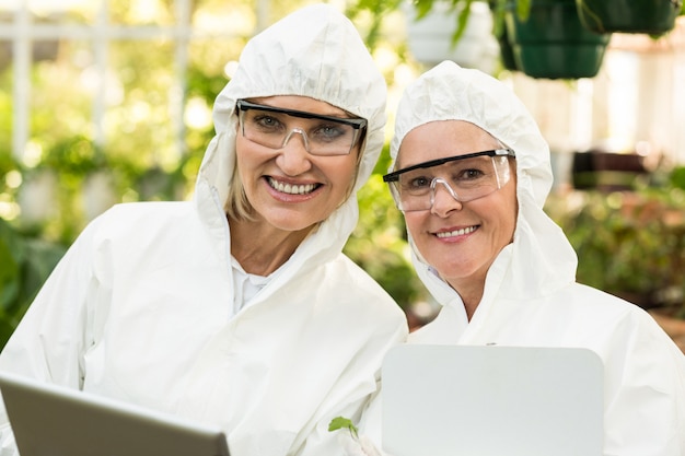 Sonriendo compañeras de trabajo vistiendo traje limpio en invernadero