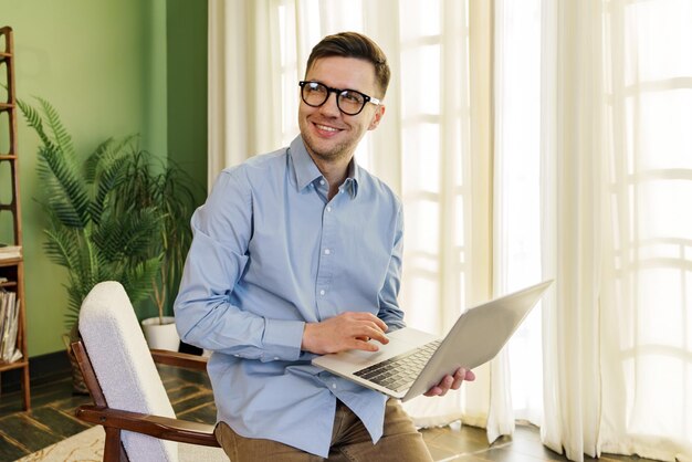 Sonriendo con confianza un profesional en una camisa azul se encuentra con su portátil su positivo