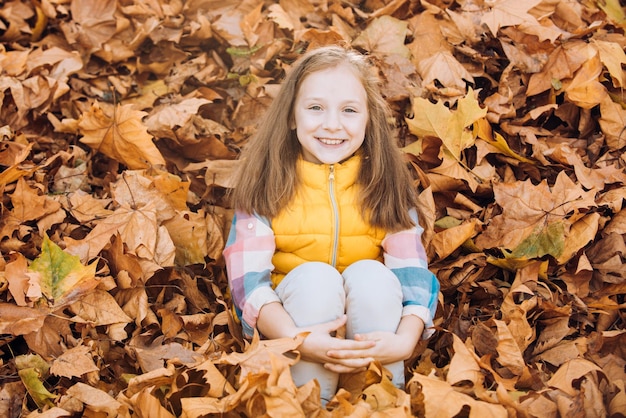 Sonriendo y divirtiéndose en el parque de la ciudad de otoño Niño sentado en hojas Adorable niña con otoño le