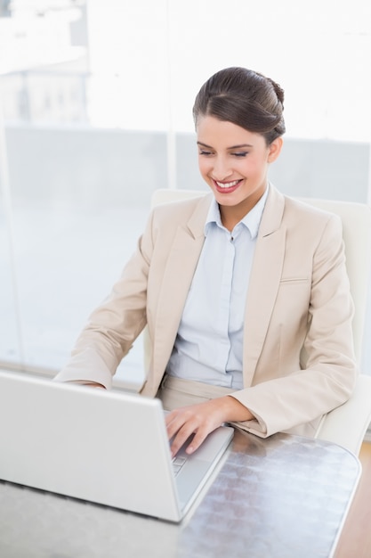 Sonriendo a la empresaria cabelluda marrón elegante que usa una computadora portátil