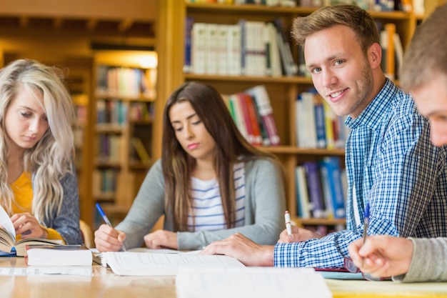 Sonriendo estudiante masculino con amigos en el mostrador de la biblioteca