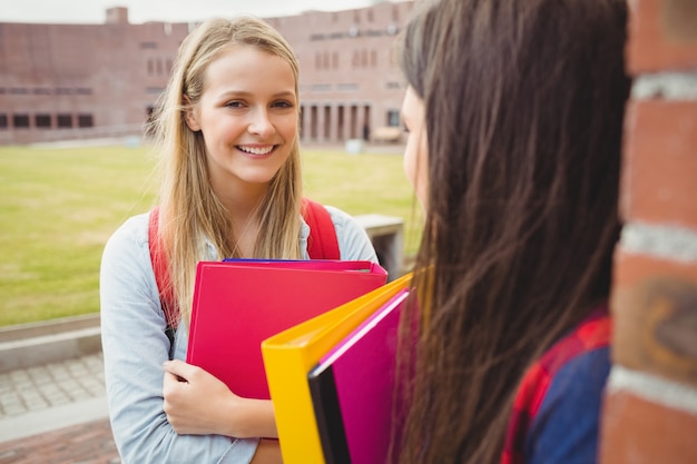 Sonriendo estudiantes hablando al aire libre en la universidad