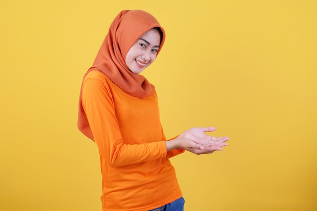 Sonriendo feliz mujer asiática algo en la mano y presentarlo sobre fondo de banner amarillo claro con hijab