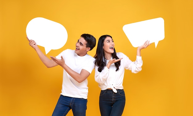 Sonriendo feliz pareja asiática sosteniendo bocadillos en blanco sobre amarillo.