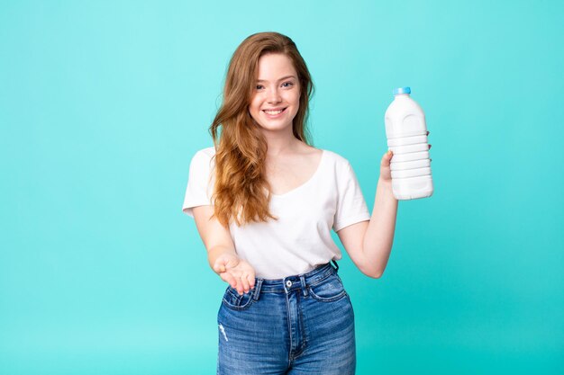 Sonriendo felizmente con amabilidad y ofreciendo y mostrando un concepto y sosteniendo una botella de leche