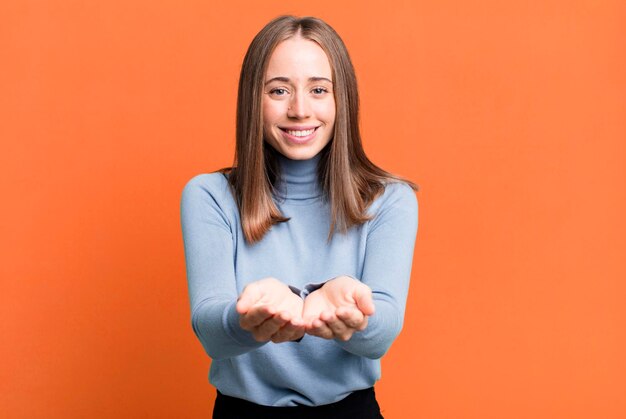 Foto sonriendo felizmente con una mirada amistosa, segura y positiva, ofreciendo y mostrando un objeto o concepto.