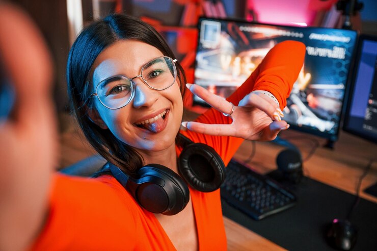 Foto sonriendo haciendo gesto de victoria y haciendo selfie joven hermoso juego streamer está en el interior con pc