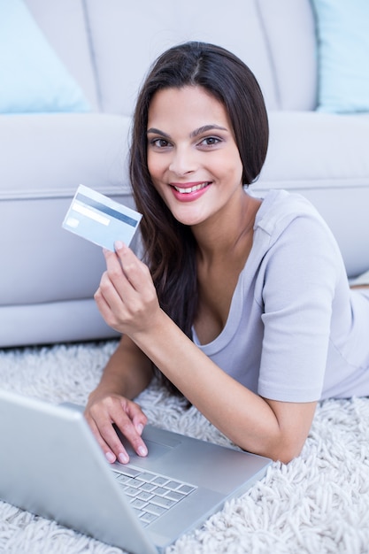 Sonriendo hermosa morena tirado en el piso y haciendo compras en línea