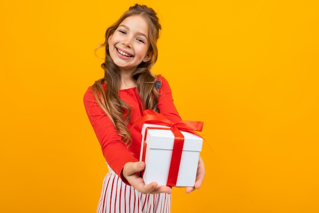 Sonriendo hermosa niña caucásica sostiene una caja con un regalo de cumpleaños en un estudio amarillo