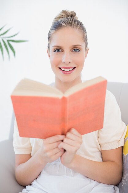 Sonriendo el libro de lectura modelo fresco sentado en el sofá