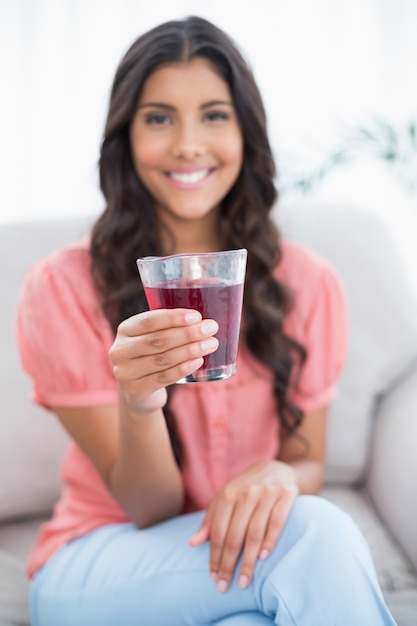 Sonriendo linda morena sentada en el sofá con vaso de jugo