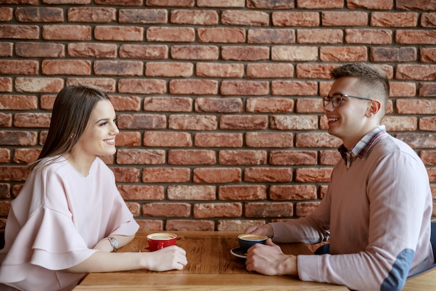 Sonriendo linda pareja vestida elegante charlando y tomando café en la cafetería