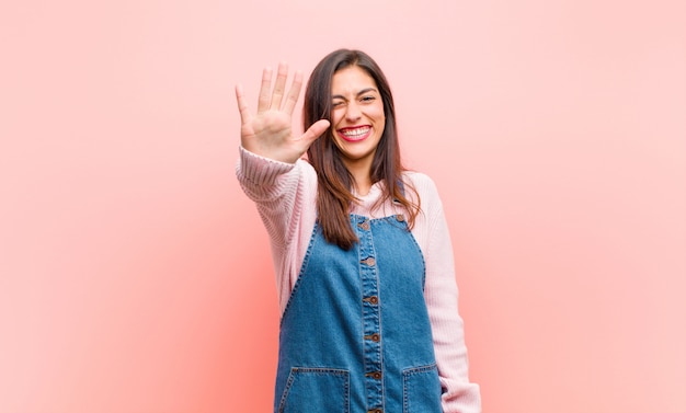 sonriendo y luciendo amigable, mostrando el número cinco o quinto con la mano hacia adelante, contando hacia atrás