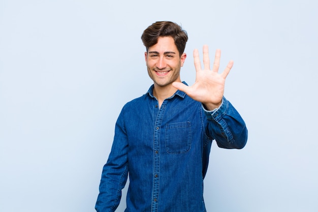 sonriendo y luciendo amigable, mostrando el número cinco o quinto con la mano hacia adelante, contando