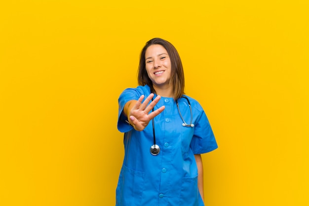 Sonriendo y luciendo amigable, mostrando el número cuatro o cuarto con la mano hacia adelante, contando hacia atrás aislado en la pared amarilla