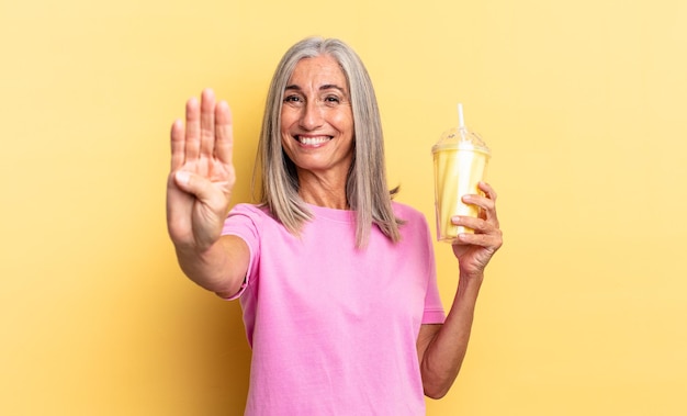 Sonriendo y luciendo amigable, mostrando el número cuatro o cuarto con la mano hacia adelante, contando hacia atrás y sosteniendo un batido.