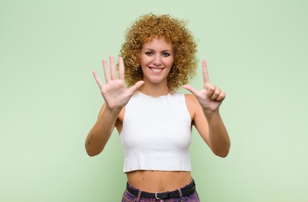 sonriendo y luciendo amigable, mostrando el número siete o séptimo con la mano hacia adelante, contando hacia atrás