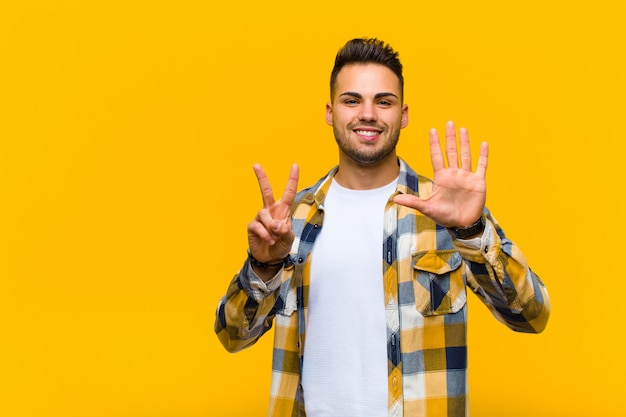 sonriendo y luciendo amigable, mostrando el número siete o séptimo con la mano hacia adelante, contando