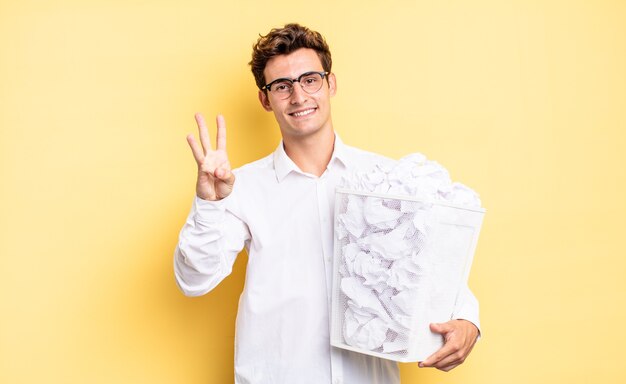 Sonriendo y luciendo amigable, mostrando el número tres o tercero con la mano hacia adelante, contando hacia atrás. concepto de papel de basura