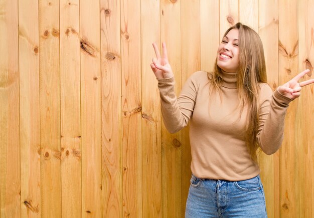 sonriendo y luciendo feliz, amigable y satisfecho, gesticulando victoria o paz con ambas manos