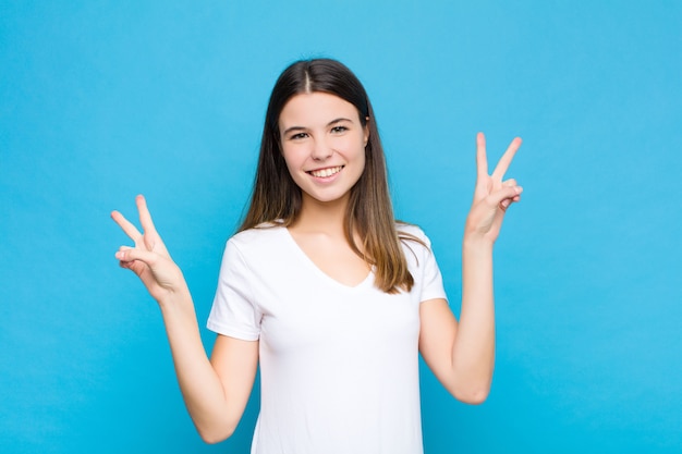 sonriendo y luciendo feliz, amigable y satisfecho, gesticulando victoria o paz con ambas manos