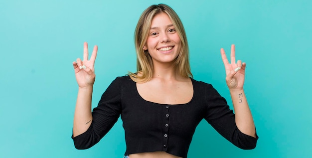 Sonriendo y luciendo feliz, amistoso y satisfecho, gesticulando victoria o paz con ambas manos.