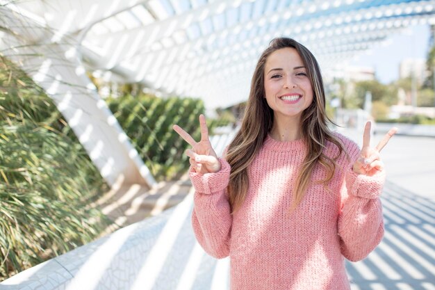 Sonriendo y luciendo feliz, amistoso y satisfecho, gesticulando victoria o paz con ambas manos.