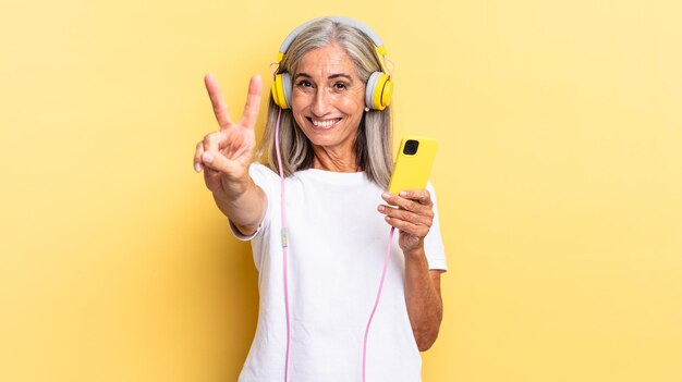 Sonriendo y luciendo feliz, despreocupado y positivo, gesticulando victoria o paz con una mano con auriculares