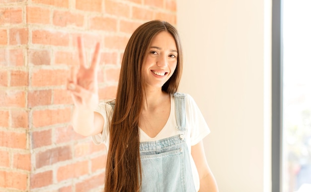 sonriendo y luciendo feliz, despreocupado y positivo, gesticulando victoria o paz con una mano