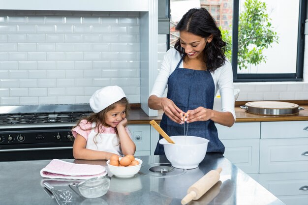 Sonriendo madre e hija rompiendo huevos