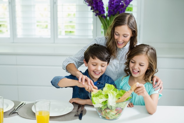 Sonriendo la madre y los niños tazón de ensalada en la cocina