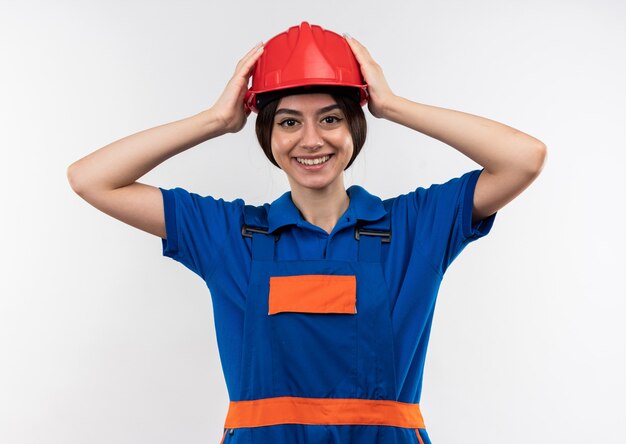 Sonriendo mirando a la cámara joven constructor mujer en uniforme agarró la cabeza